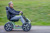 A blog banner image with a man in a green mobility scooter, zooming along a path in a park.